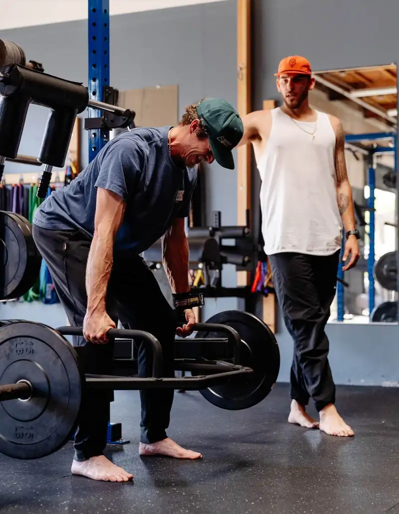 An athlete setting up a trap-bar pull while a second athlete spots from behind